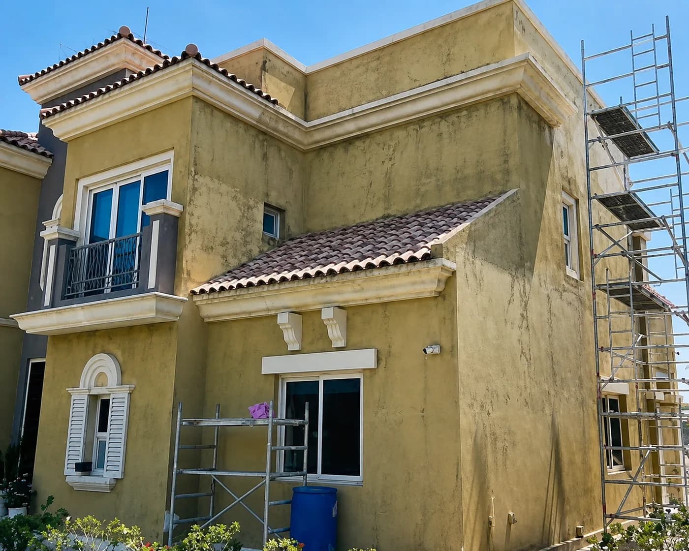 A villa elevation with faded yellow paint and dark staining running down the render