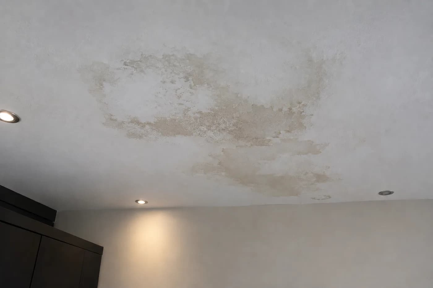 A bedroom ceiling with a large brown water stain spreading across it