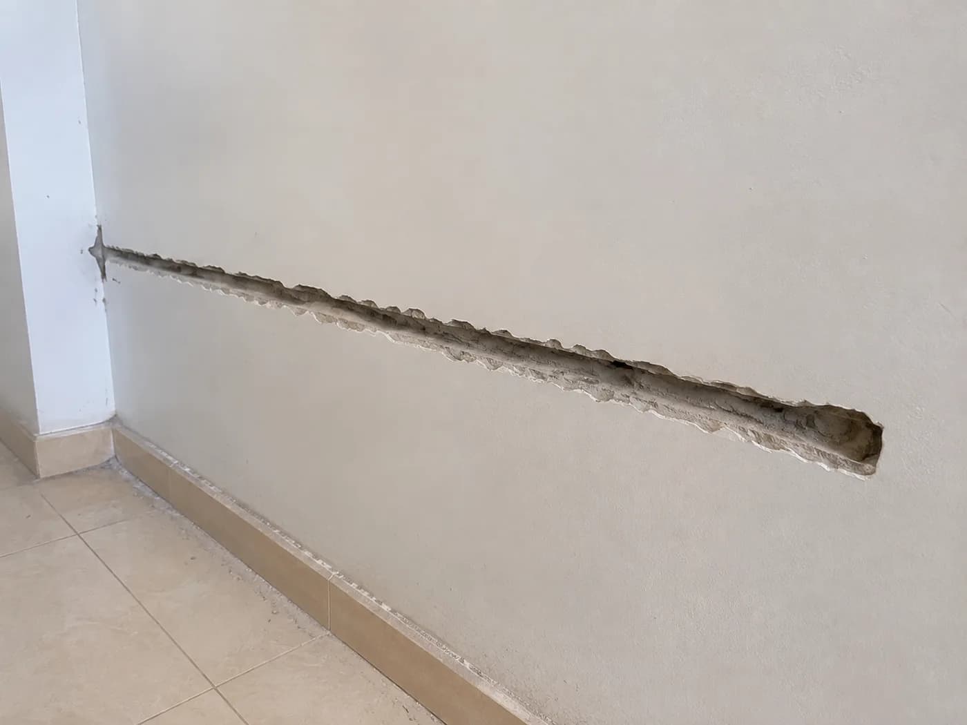 A wall crack opened out into a groove, ready to be cleaned and filled